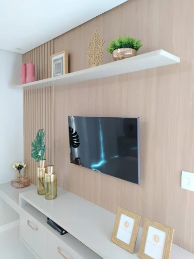 Painel ripado de madeira clara com rack branco e prateleira suspensa na sala