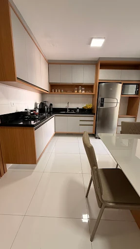 Cozinha planejada em L com armários off-white, detalhes em madeira e bancada preta